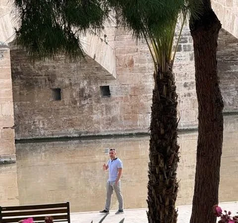 Jeton Toska walking along a river promenade under palm trees